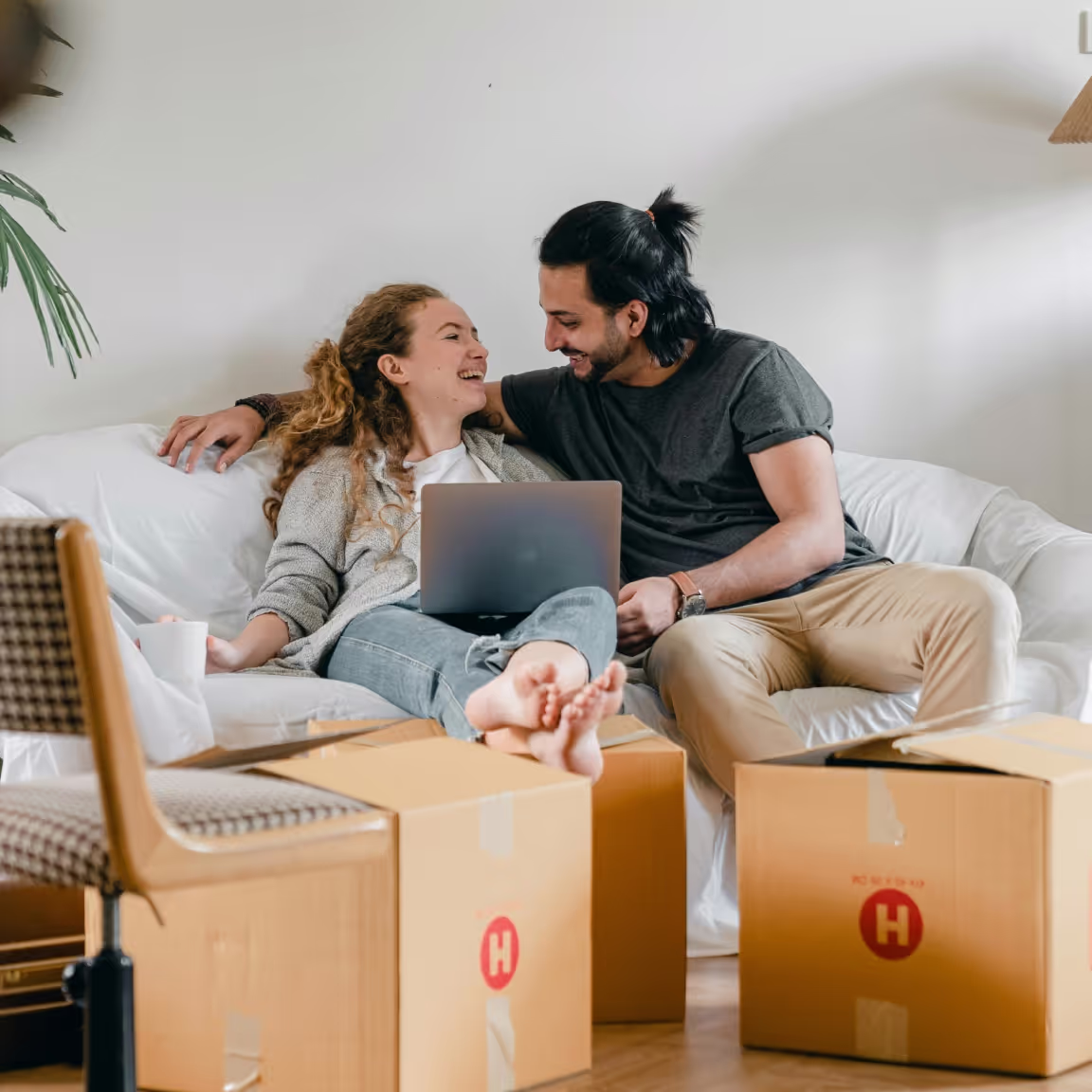 Photo of a smiling couple sitting on a couch with moving boxes around, representing the satisfaction of a clean, organised space after junk removal.